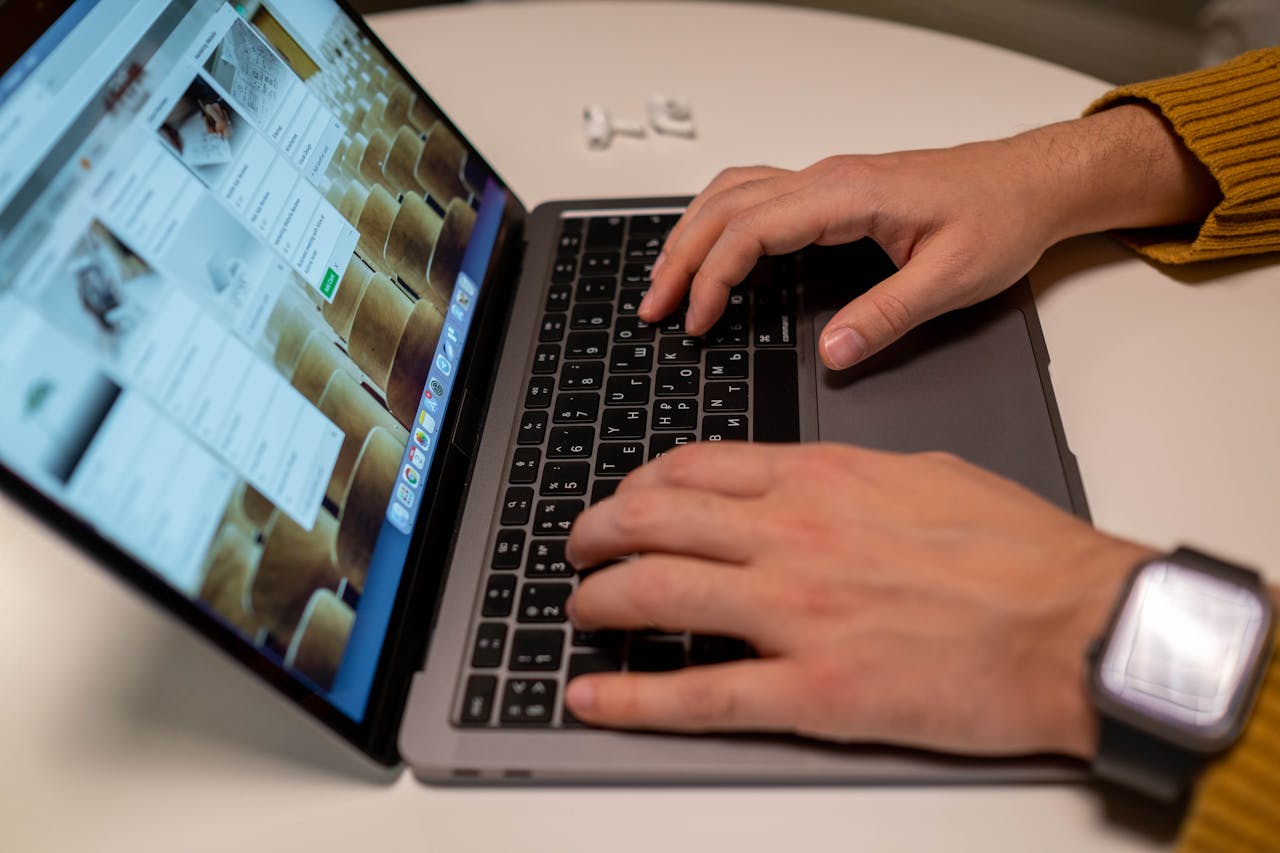 Close-up of hands typing on a laptop with a smartwatch in an indoor setting.