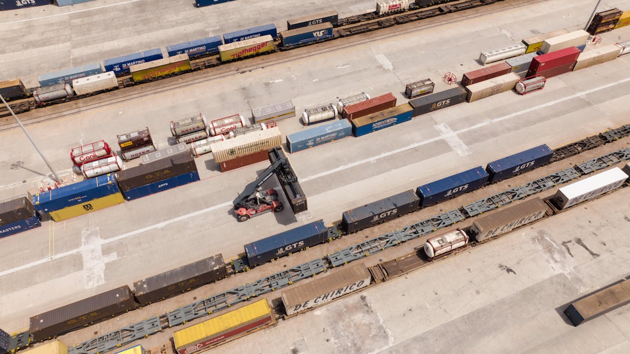 High angle drone shot of a logistics hub with stacked containers and a forklift.