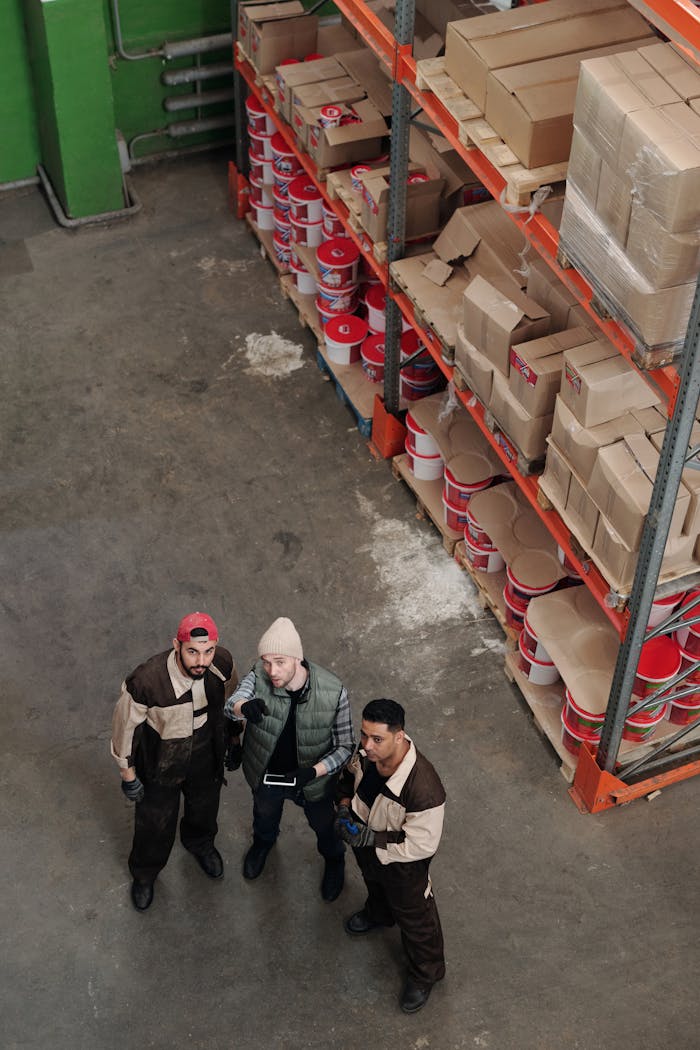Workers in a warehouse discussing logistics near shelves filled with packages and products.
