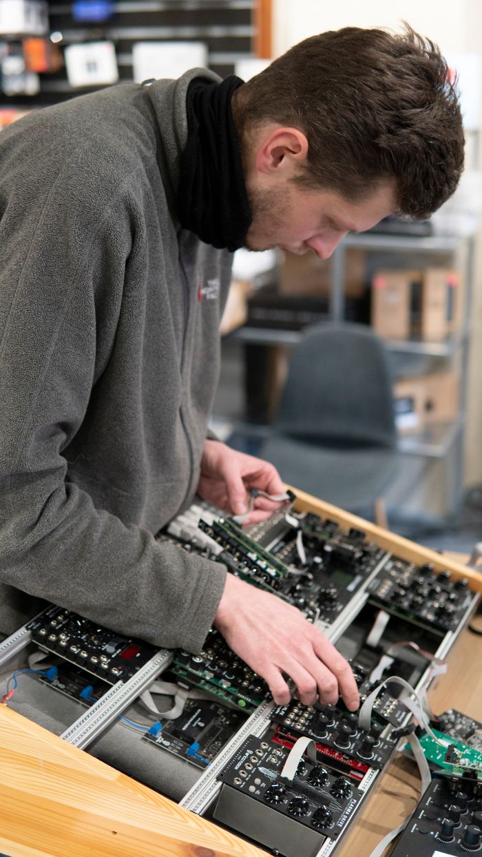 Man in a gray sweater assembling modular synthesizer in a recording studio.